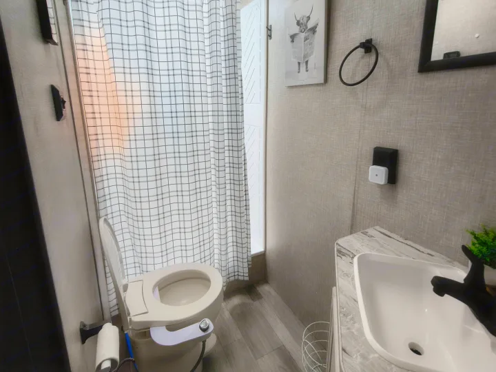 Modern RV rental bathroom: toilet with bidet, checkered shower, sleek sink, and cow art. Functional and stylish.. Jayco Jay Flight 2023