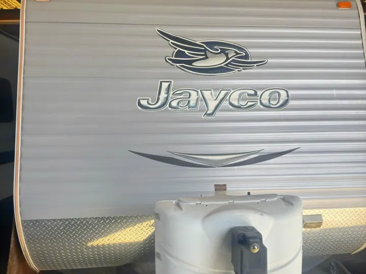 Front view of a grey Jayco RV, featuring a prominent logo, propane tank, and diamond plate rock guard, ideal for your next rv rental.. Jayco Jay Flight 2015