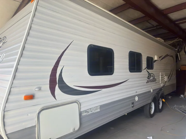 Side view of a grey and white Jay Flight travel trailer, perfect for an RV rental adventure. Features windows & graphics.. Jayco Jay Flight 2015