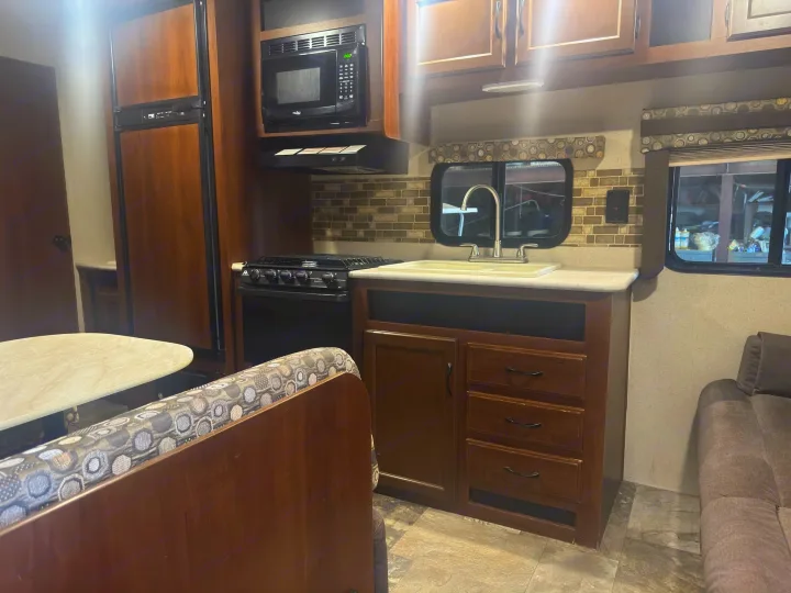 This RV rental boasts a full kitchen: fridge, microwave, stove, sink, ample cabinets, and a cozy dinette with patterned seating.. Jayco Jay Flight 2015