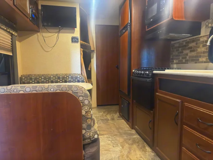 RV rental interior: dinette with patterned cushions, kitchenette featuring microwave, stove, and fridge. Wood cabinetry throughout.. Jayco Jay Flight 2015