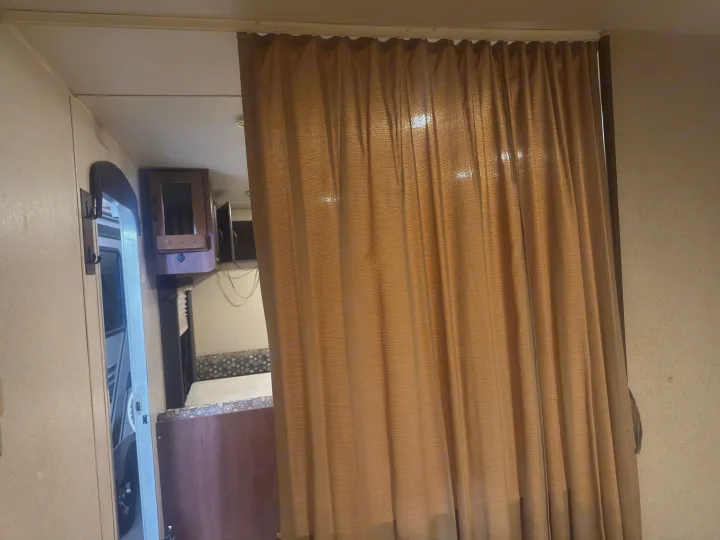 RV rental interior: A drawn brown curtain forms a privacy partition, with cabinets, a dinette, and a doorway visible.. Jayco Jay Flight 2015