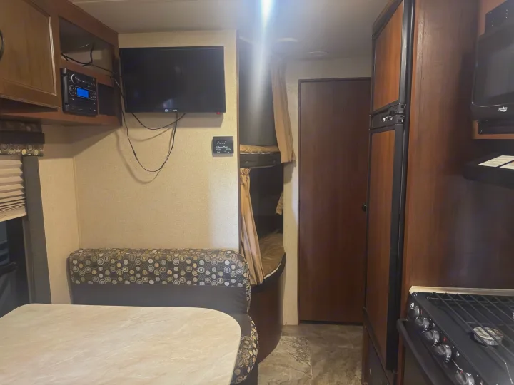 RV rental interior featuring a cozy dinette, well-equipped kitchen with stove and fridge, entertainment system, and bunk beds.. Jayco Jay Flight 2015