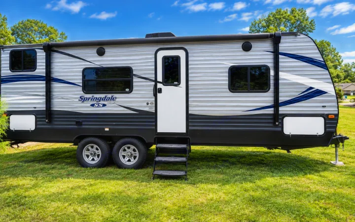 A stylish gray Springdale travel trailer with blue accents, ideal for rv rental, sits on green grass under a bright sky.. Keystone RV Springdale SSR 2018