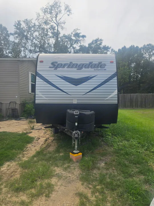 Springdale RV rental: A grey travel trailer with blue accents, parked on grass next to a home.. Keystone RV Springdale SSR 2018