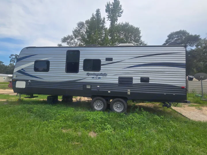 Parked Springdale SS travel trailer, silver and black, for an rv rental. Located on grass with trees behind it.. Keystone RV Springdale SSR 2018