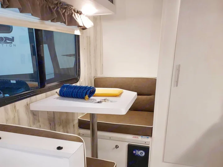 Cozy rv rental interior: dinette with table, seating, window, and storage. Keys and a blue hose are on the table.. Travel Lite Rove Lite 2023