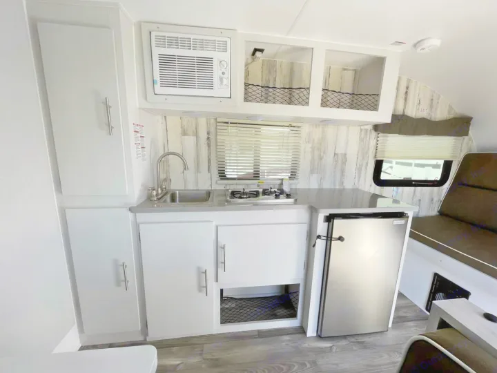 Compact kitchen in this RV rental: stainless fridge, sink, stovetop, and AC unit, with a wood accent wall.. Travel Lite Rove Lite 2023