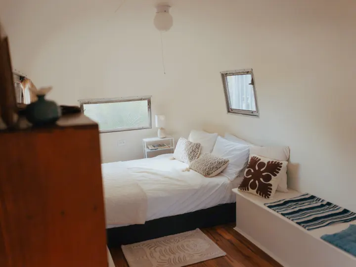 Cozy RV rental bedroom with a comfortable bed, white bedding, patterned pillows, and natural light from unique windows.. Airstream Land Yacht 1960