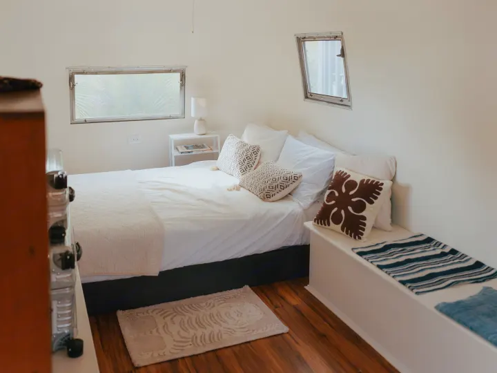 Cozy RV rental bedroom with white bed, patterned pillows, windows, and wooden floor for a compact stay.. Airstream Land Yacht 1960