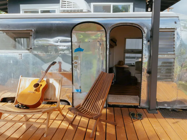 Cozy Airstream **RV rental** with an open door revealing its interior, a guitar, and wooden chairs on a sunny deck.. Airstream Land Yacht 1960