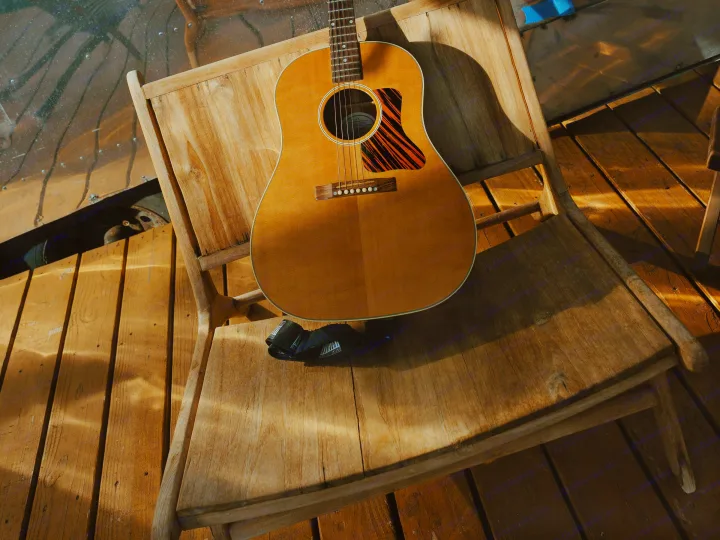 An acoustic guitar rests on a sunlit wooden chair next to an RV rental. Perfect for music on your road trip adventure.. Airstream Land Yacht 1960
