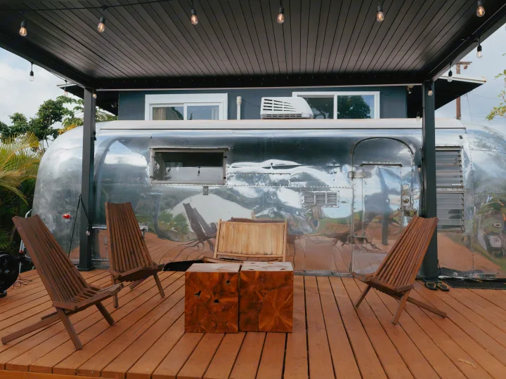 Unique Airstream RV rental with a wooden deck, lounge chairs, cube tables, and string lights for a glamping stay.. Airstream Land Yacht 1960