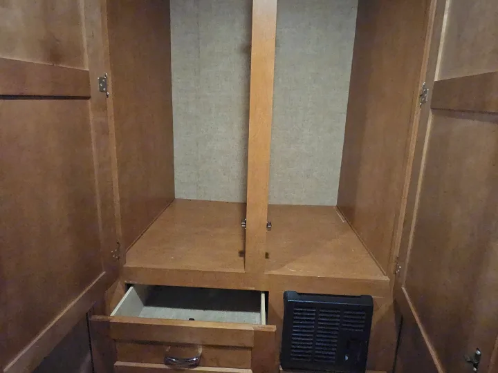 RV rental interior: an open wooden closet with a shelf, partially open drawer, and a black floor vent for practical storage.. Winnebago Minnie Winnie 2018