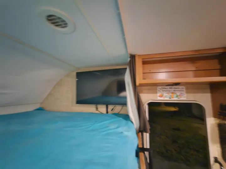 RV rental interior: a cozy bed, wall-mounted TV, overhead cabinets, and ceiling vent visible for a comfortable trip.. Winnebago Minnie Winnie 2018