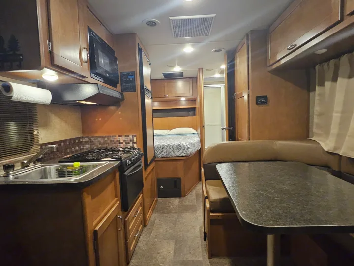 An inviting RV rental interior: kitchen with sink, stove, dinette, and a comfy rear bed for your travels.. Winnebago Minnie Winnie 2018