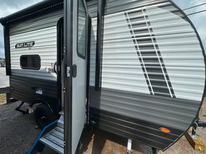 Grey & black travel trailer RV rental, side view with open door, steps, and awning. Ready for your next adventure!. Sunlite 13BHLTD 2027
