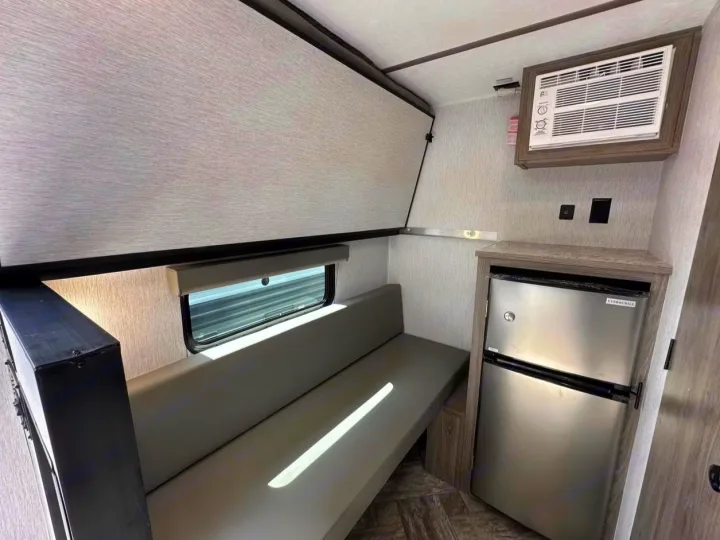 Inside this RV rental: compact interior with bench seating, fold-up bunk, mini-fridge, and wall AC for your journey.. Sunlite 13BHLTD 2027