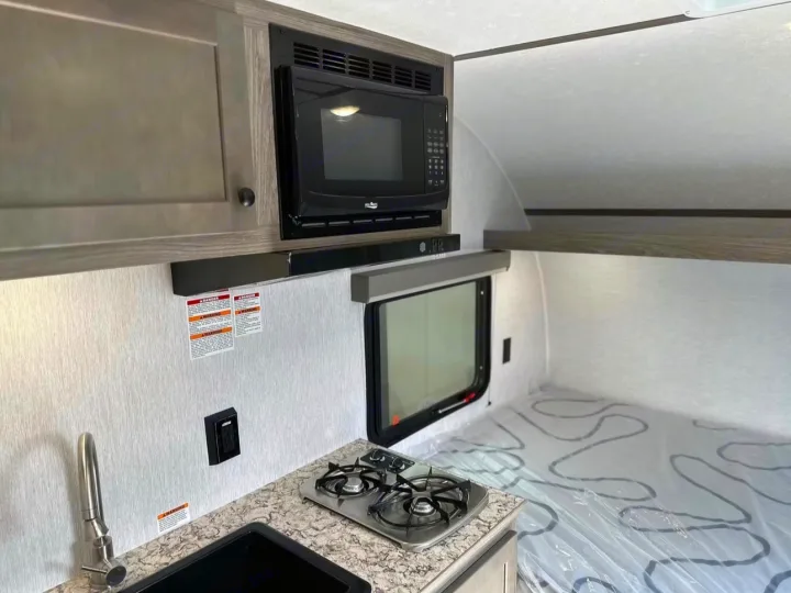 Inside this rv rental, a compact kitchenette with sink, stove, and microwave is next to a bed with a plastic-covered mattress.. Sunlite 13BHLTD 2027