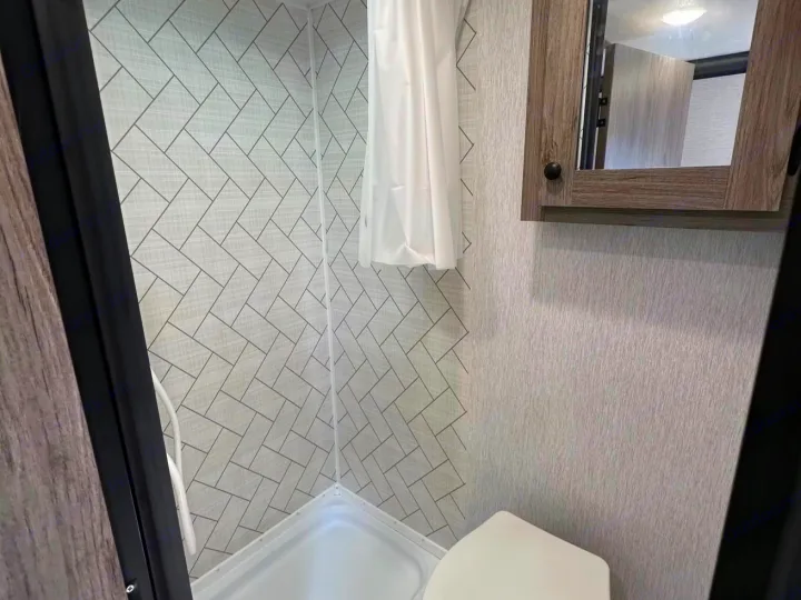 Compact RV rental bathroom with a clean tiled shower, toilet, and mirrored cabinet. Ideal for your travel journeys.. Sunlite 13BHLTD 2027