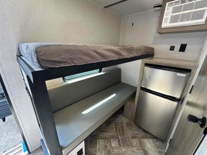 RV rental interior: cozy bunk bed, grey bench seating, mini-fridge, and AC unit. Compact living for adventure.. Sunlite 13BHLTD 2027