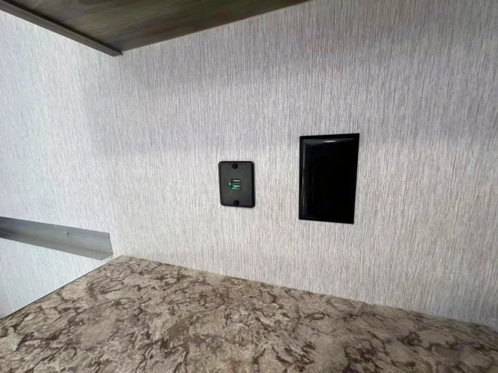 This RV rental interior shows a grey textured wall with a dual USB charger (lit green) and a black power outlet above a speckled counter.. Sunlite 13BHLTD 2027