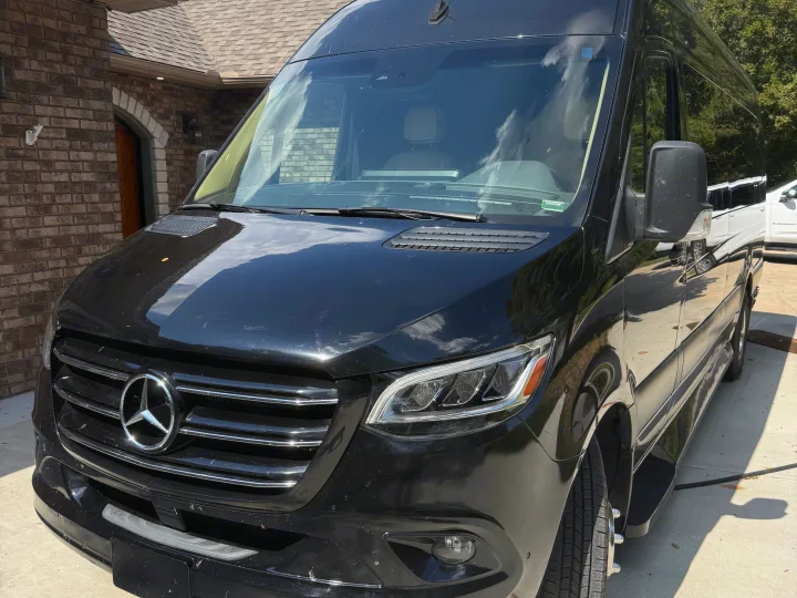 Front view of a sleek black Mercedes-Benz Sprinter van, a popular choice for rv rental, parked in a sunny driveway.. Midwest Automotive Designs Luxe Cruiser 2021