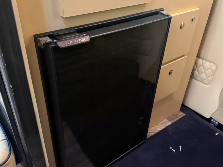 Black Nov Kool compact refrigerator, latched shut, within an RV rental's light-colored interior cabinetry.. Midwest Automotive Designs Luxe Cruiser 2021