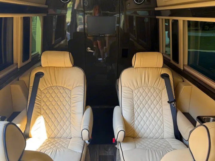 Plush cream captain's chairs with diamond stitching in a luxurious RV rental interior, offering spacious and comfortable travel.. Midwest Automotive Designs Luxe Cruiser 2021