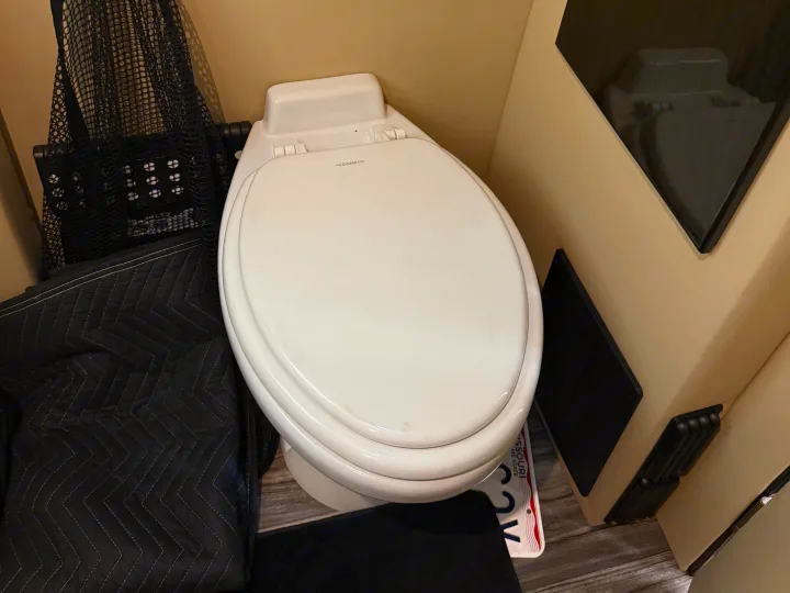 RV rental: A Dometic toilet in a compact bathroom. Features include a black quilted cover and a Missouri license plate on the floor.. Midwest Automotive Designs Luxe Cruiser 2021