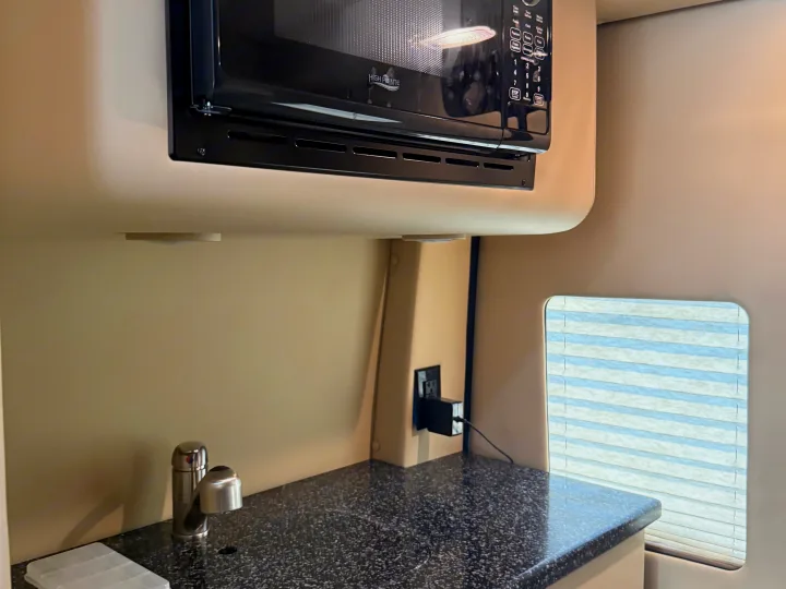 RV rental kitchen showing a High Pointe microwave, speckled counter with sink, outlet, and window with blinds.. Midwest Automotive Designs Luxe Cruiser 2021