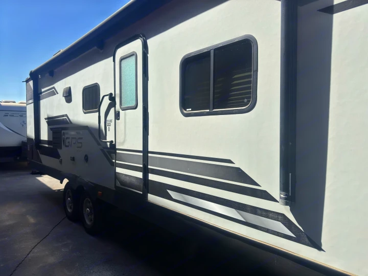 Exterior side view of a modern gray travel trailer RV rental with black stripe graphics, a door, and two windows.. Starcraft GPS 2018