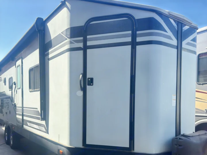 Side view of a light gray RV rental/travel trailer with black stripes, multiple doors, windows, and an awning visible.. Starcraft GPS 2018