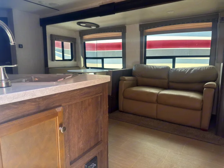 RV rental interior view: kitchen sink, light-colored sofa, and dining area. Large windows show distinct red and grey striped patterns outside.. Starcraft GPS 2018