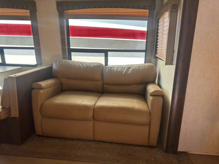 This inviting RV rental interior features a cozy beige sofa, windows with shades, and a partial view of a dinette on carpet.. Starcraft GPS 2018