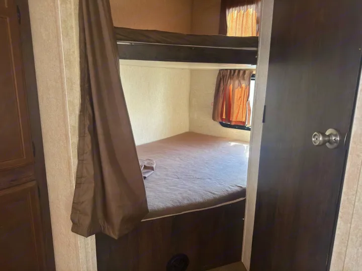 RV rental bunk bed area with a lower mattress, upper bunk, and privacy curtains, seen from a doorway.. Starcraft GPS 2018