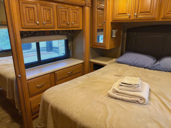 Cozy RV rental bedroom with two beds, warm wood cabinetry, a window, and fresh towels for a comfortable journey.. Thor Palazzo 2016