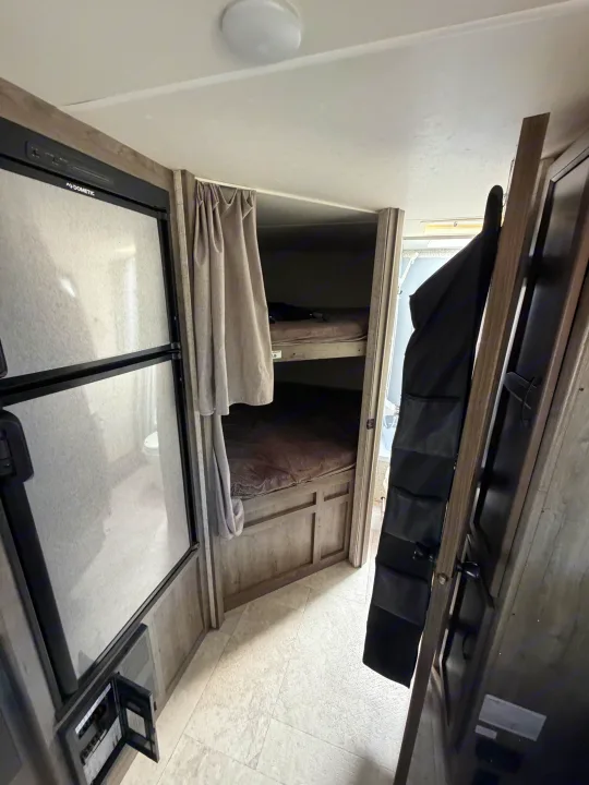 Inside this RV rental, you see a Dometic refrigerator, bunk beds with curtains, and a hanging organizer for storage.. Coachmen Apex 2020