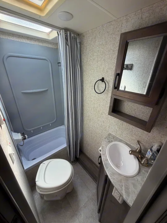 Compact RV rental bathroom: shower/tub, toilet, sink vanity with mirror. Clean and functional.. Coachmen Apex 2020