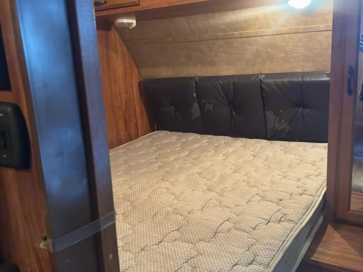 RV rental bedroom view: mattress, peeling tufted headboard, wood walls, and overhead light inside.. KZ C291IKS 2015