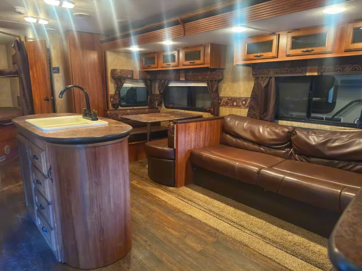 Cozy rv rental interior: kitchen island, dining booth, sofa, & bunk beds. Warm wood finishes & inviting brown tones.. KZ C291IKS 2015