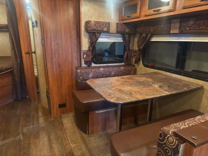 Cozy RV rental interior showcasing a dinette with patterned cushions, windows, cabinets, and a bunk bed area.. KZ C291IKS 2015
