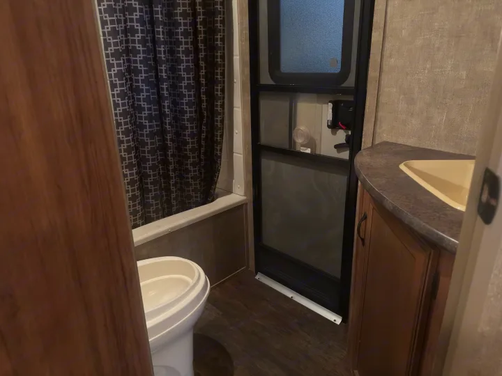 Compact RV rental bathroom with toilet, shower (geometric curtain), and functional sink vanity. Features wood-look floors and beige walls.. KZ C291IKS 2015