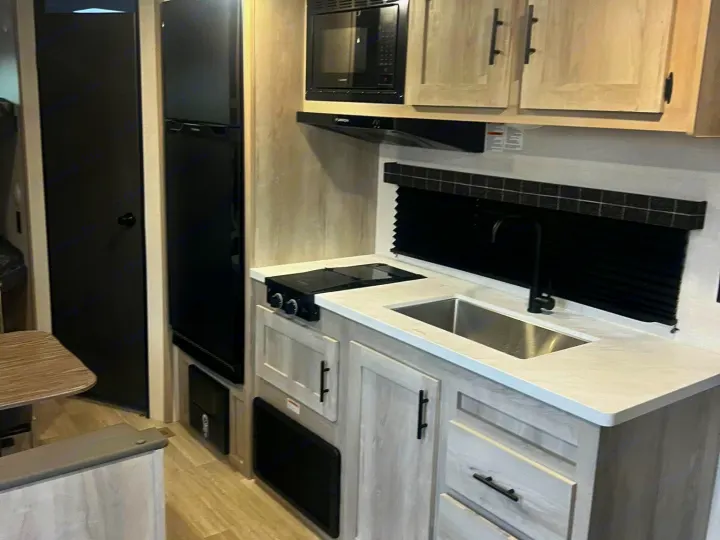 RV rental kitchen: Modern interior with light wood cabinets, a sink, black appliances, & counter space.. Other Other 2024