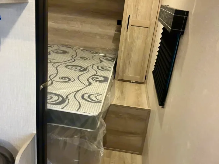 Inside an RV rental: a neat bedroom with a new mattress, overhead shelf, and built-in wardrobe for storage.. Other Other 2024