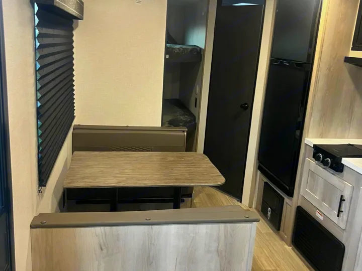 Inside this RV rental: modern dinette, kitchen with stove/fridge, and bunks. Light wood tones, bright lights. Adventure awaits!. Other Other 2024
