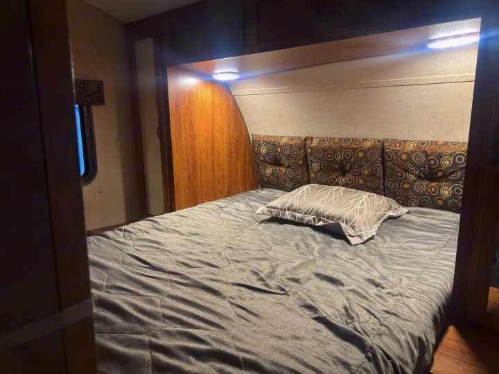 Cozy RV rental bedroom features a patterned headboard, grey comforter, and overhead lighting for comfortable travel.. KZ C250BHS 2015