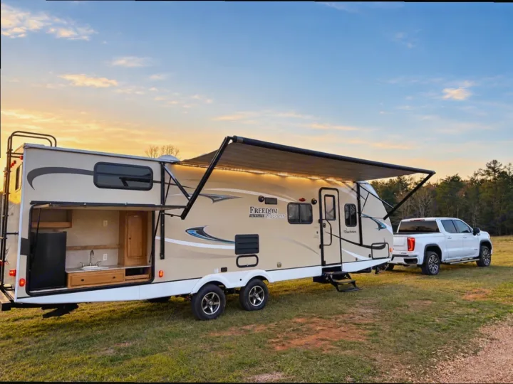 Freedom Express RV rental with open outdoor kitchen, extended awning, hitched to a white pickup truck on grass.. Coachmen Coachmen Freedom Express Ultra Lite 292BHDS 2019