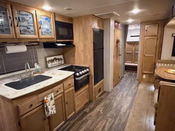 RV rental interior features a cozy kitchen, dinette, wood cabinetry, and a sign: 'Adventure Awaits!' Perfect for trips.. Coachmen Coachmen Freedom Express Ultra Lite 292BHDS 2019