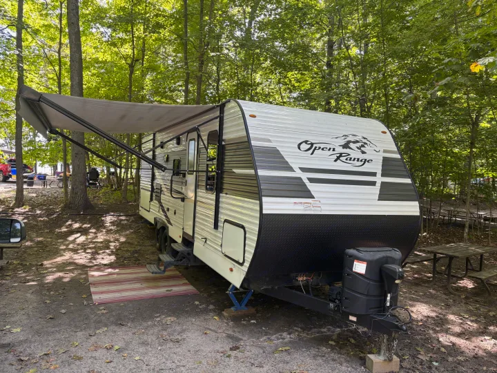 An Open Range **rv rental** parked at a wooded campground with its awning extended, surrounded by green trees and fallen leaves.. Highland Ridge RV Open Range 2022